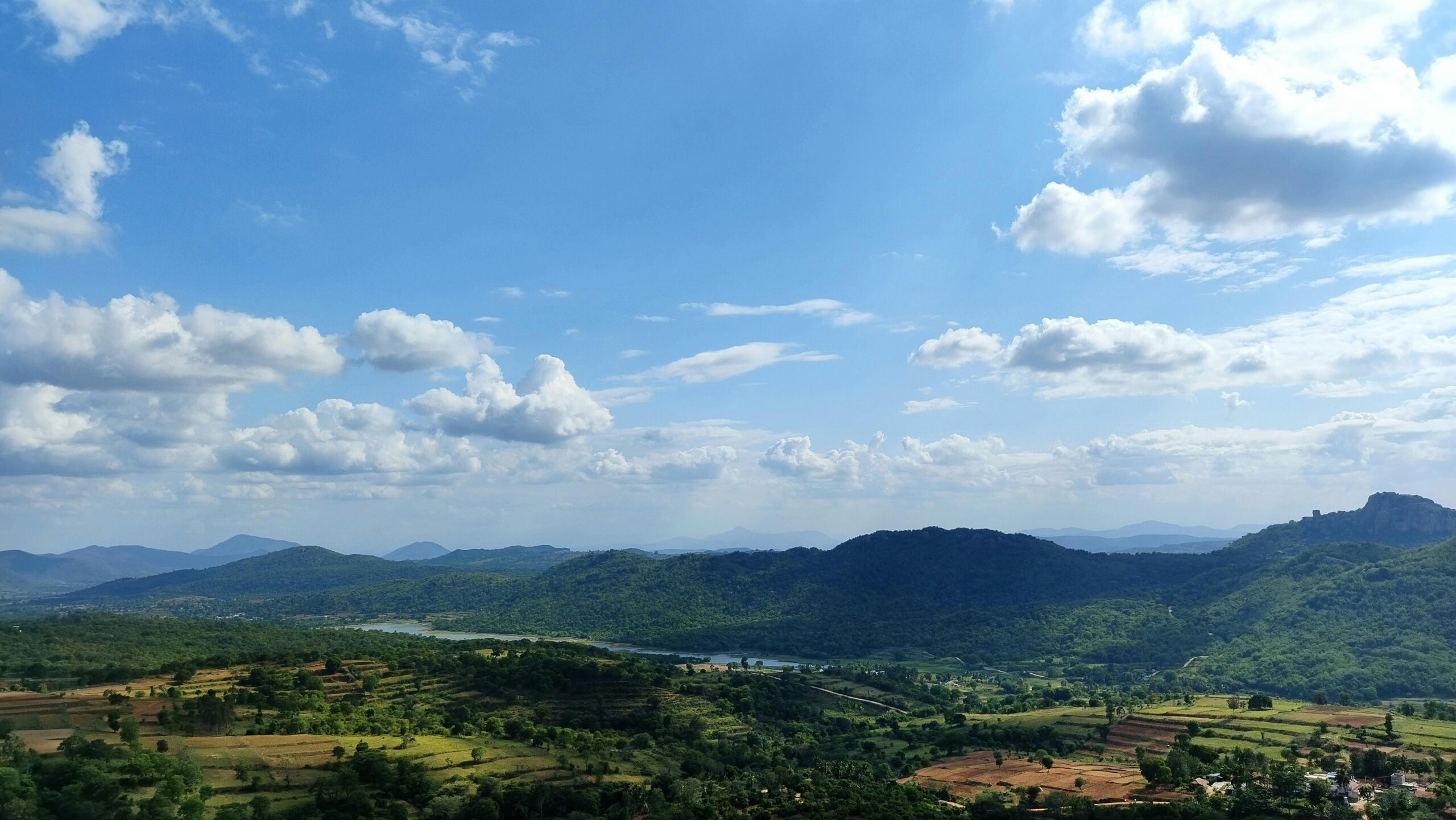 Aerial view of a vibrant, lush green landscape with hills and a wide open sky.