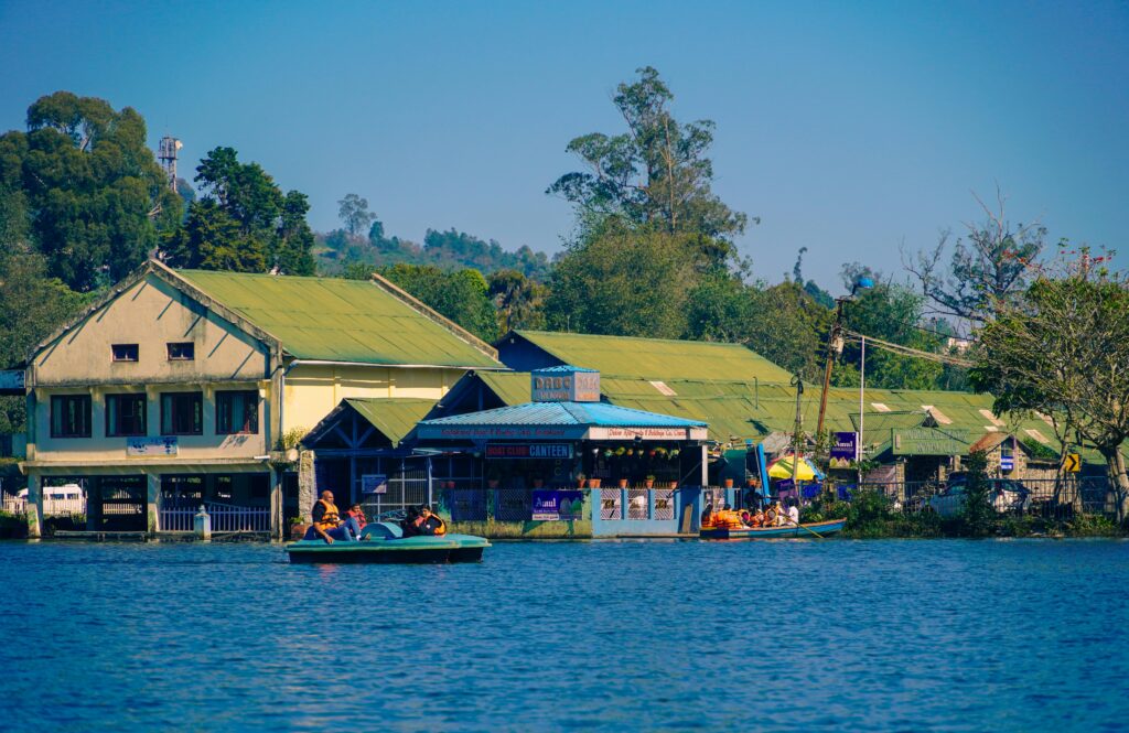 Picturesque view of boating at Kodaikanal Lake with buildings and lush greenery.